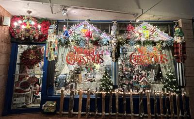 Nighttime, the Rose Tree Cottage is lit up and showing Christmas decorations hanging from their storefront ceiling